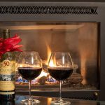 Two glasses of Red wine and wine bottle in front of fireplace along with bouquet of tulips